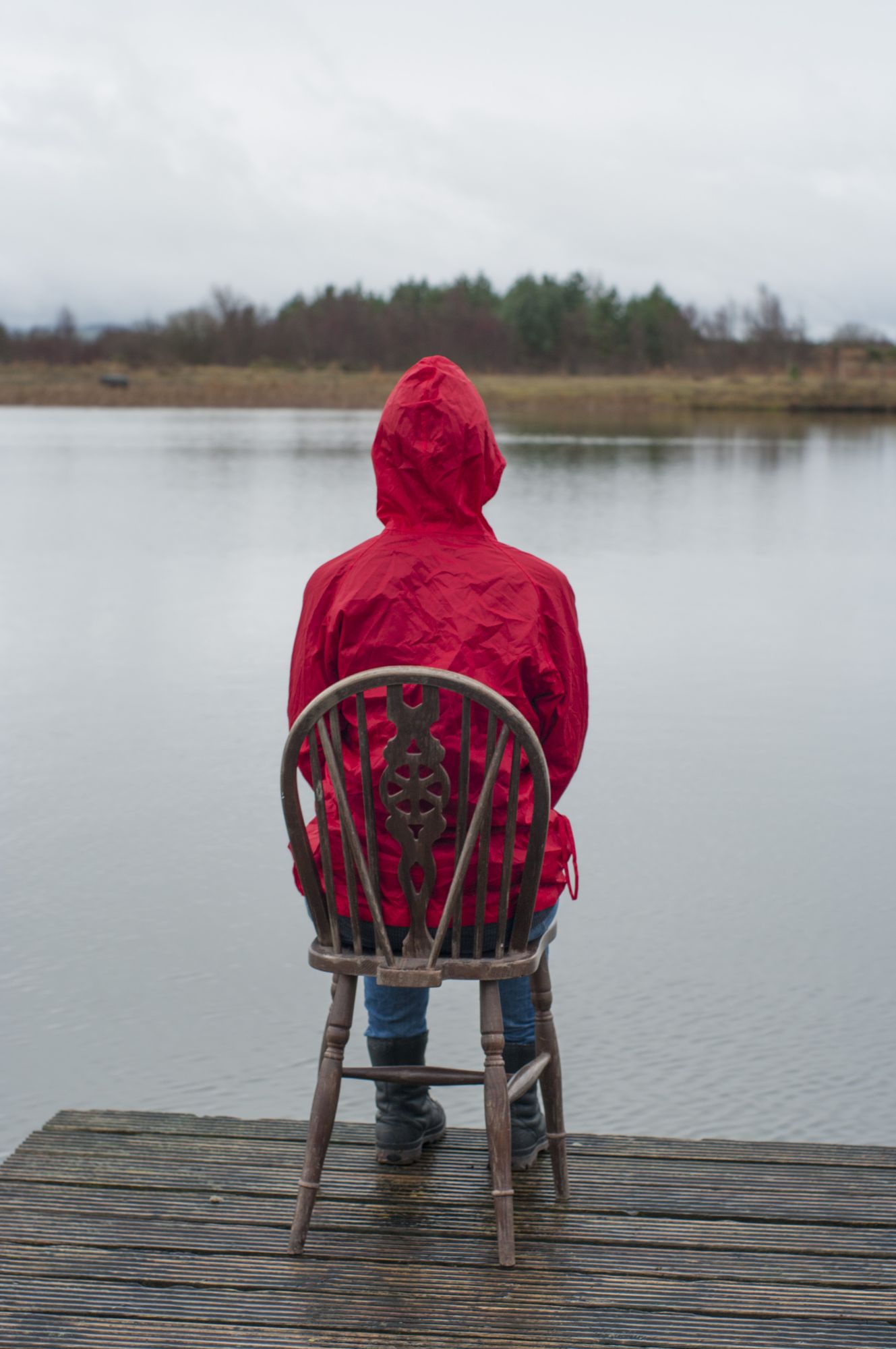 The figure in the red raincoat, seen from behind, seated before the water