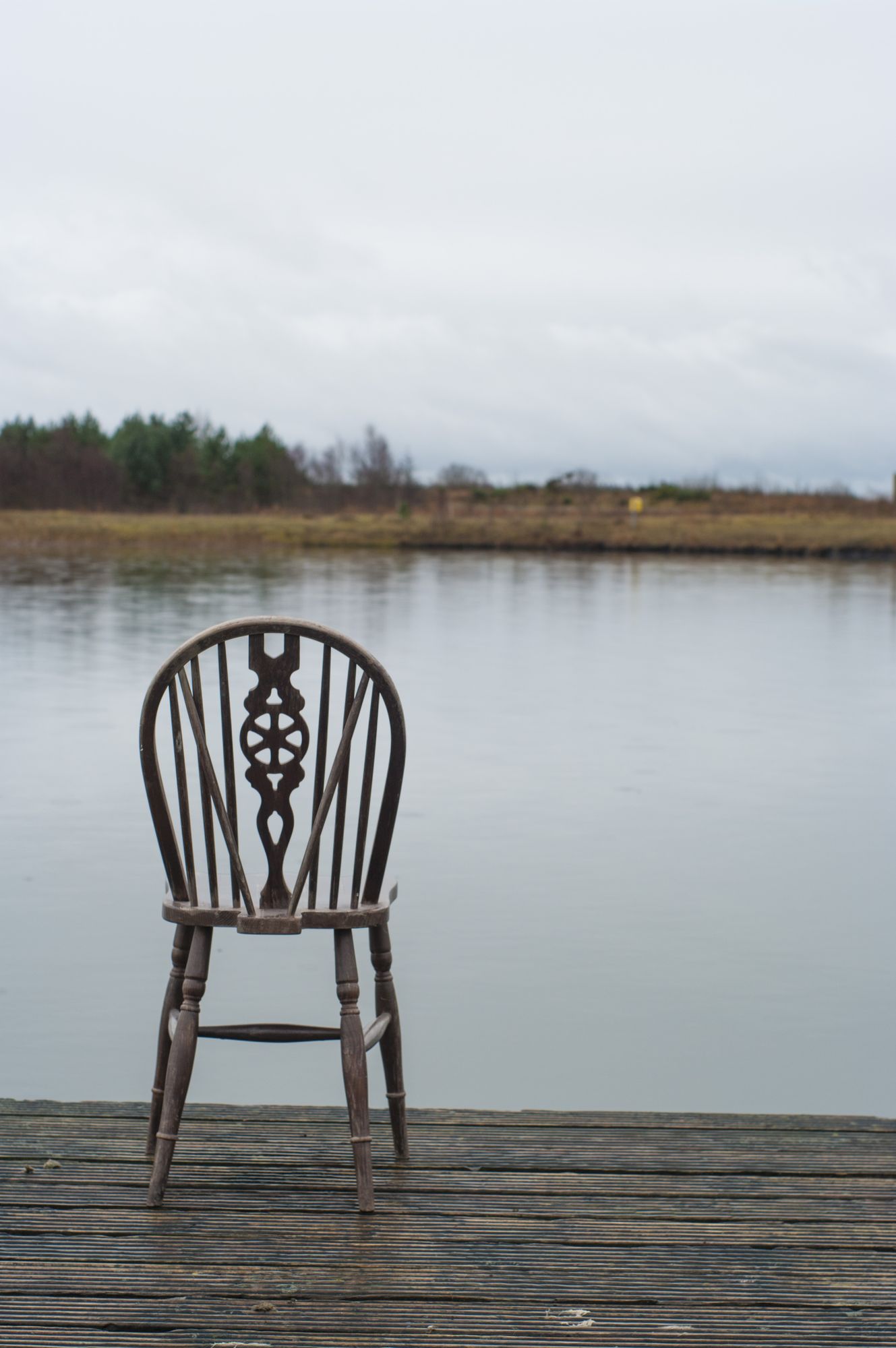 The wooden chair alone on the jetty, facing the water